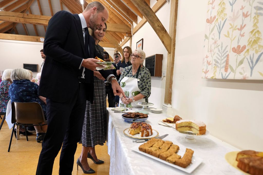 Princess of Wales and Prince William pointing at table of cake 