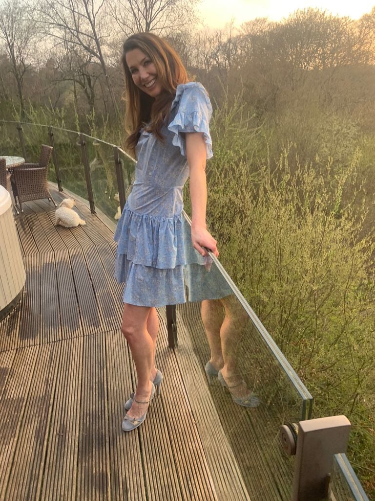 Rosie Green posing in a blue floral dress by a balcony