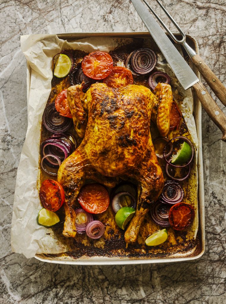 A whole roast chicken on a train surrounded by mediterean vegetables 