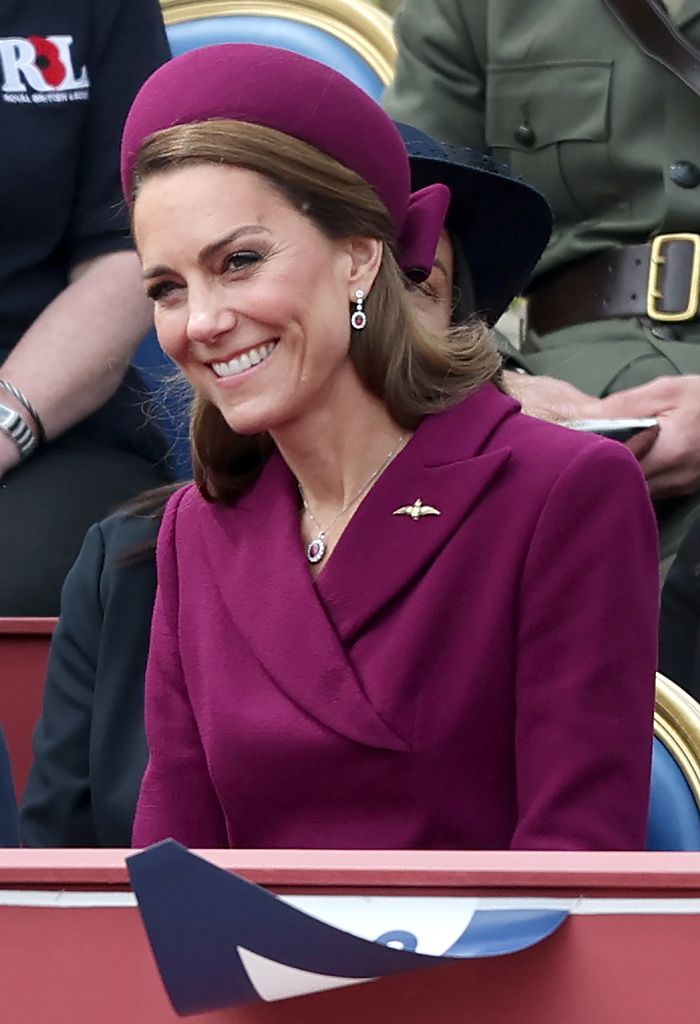 Kate tersenyum dalam gaun mantel ungu dan topi