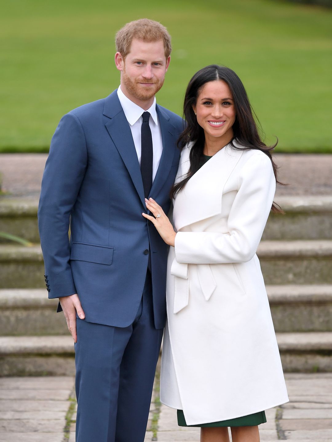 Prince Harry in a blue suit and Meghan Markle in a white overcoat