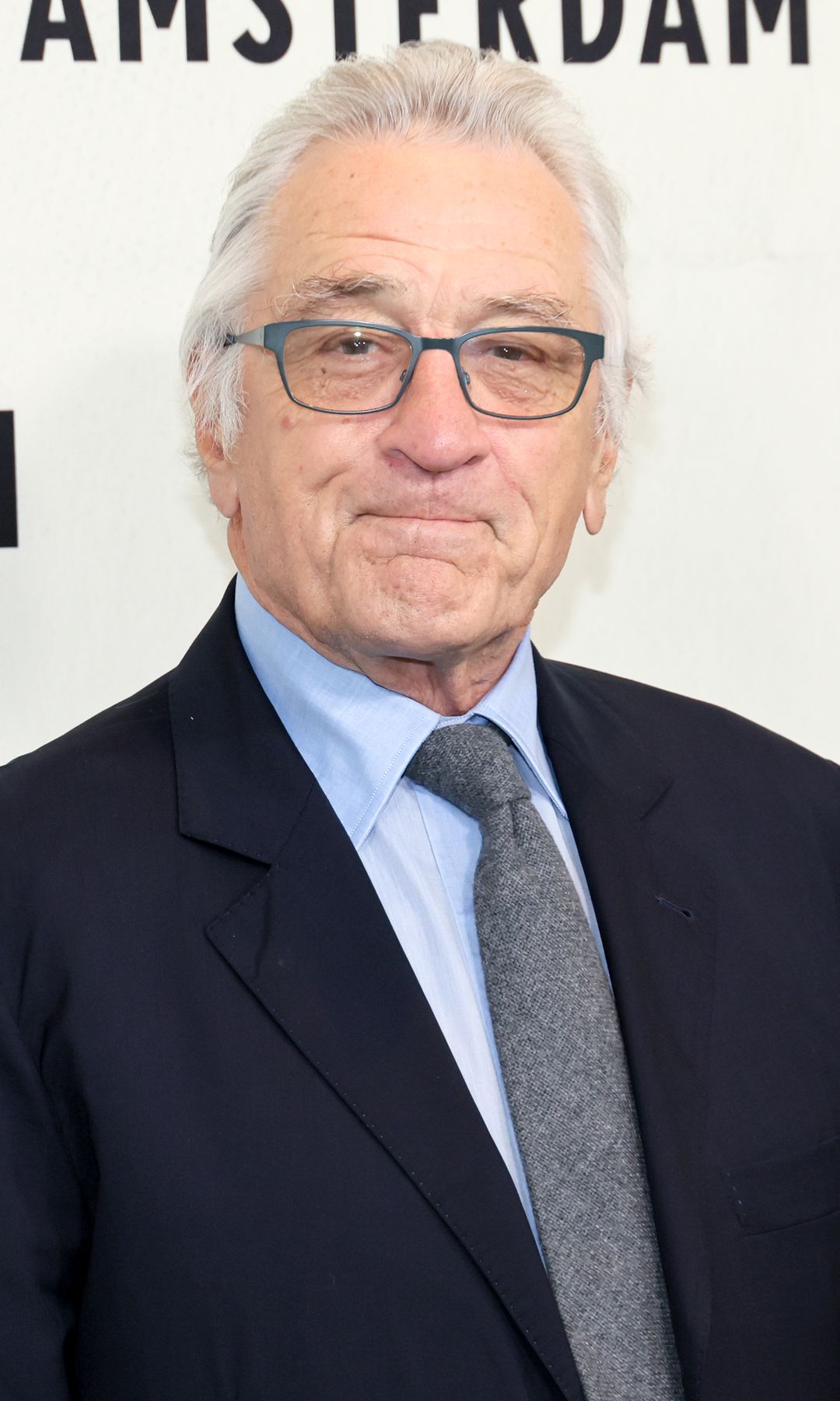 Robert De Niro in a suit and tie standing in white board at film premiere looking at photographers