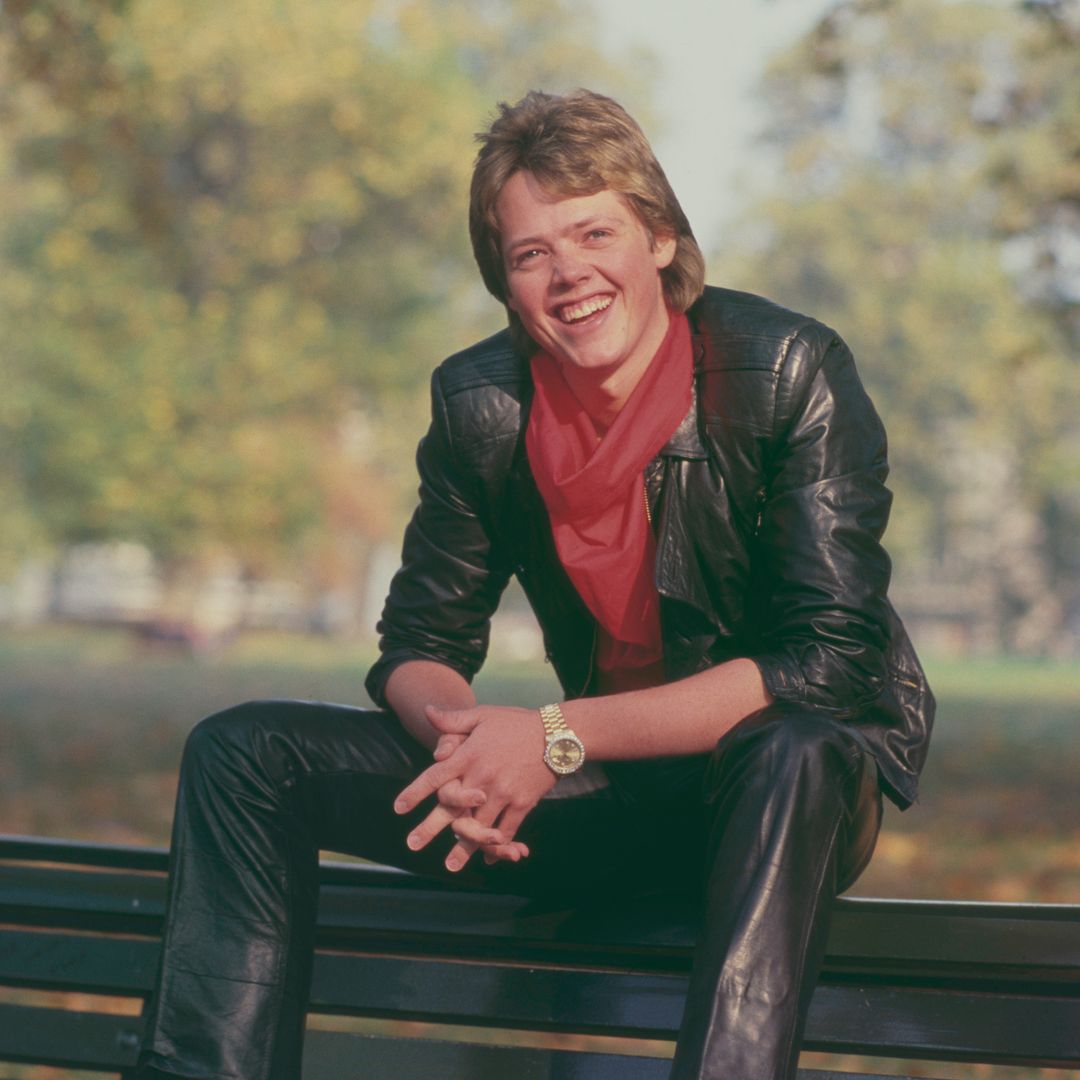 Jimmy Osmond, American singer and member of American family group The Osmonds, posed wearing a leather jacket and trousers as he sits on a bench in a park in London in October 1983